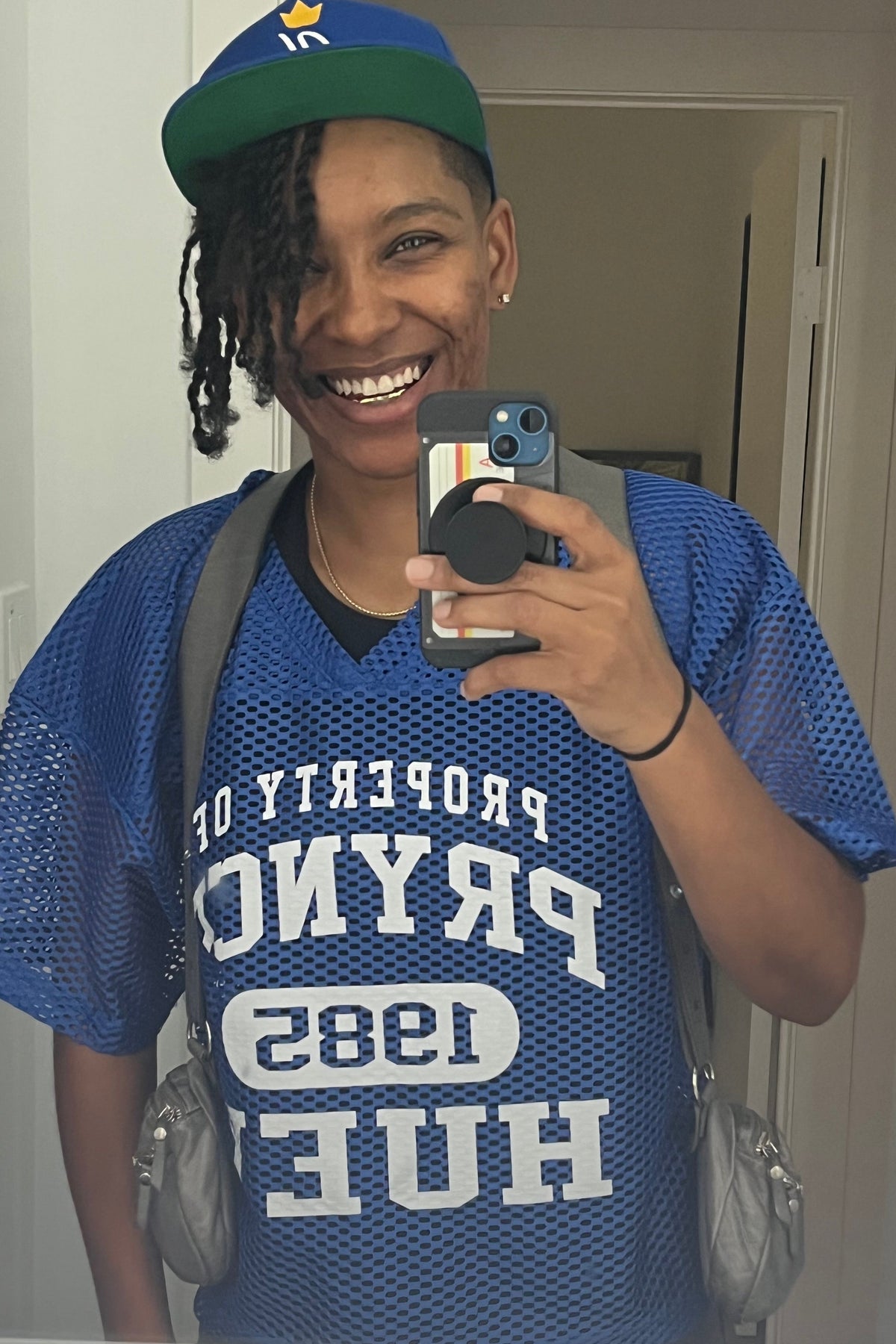 Person wearing a blue sports jersey with text, taking a mirror selfie.