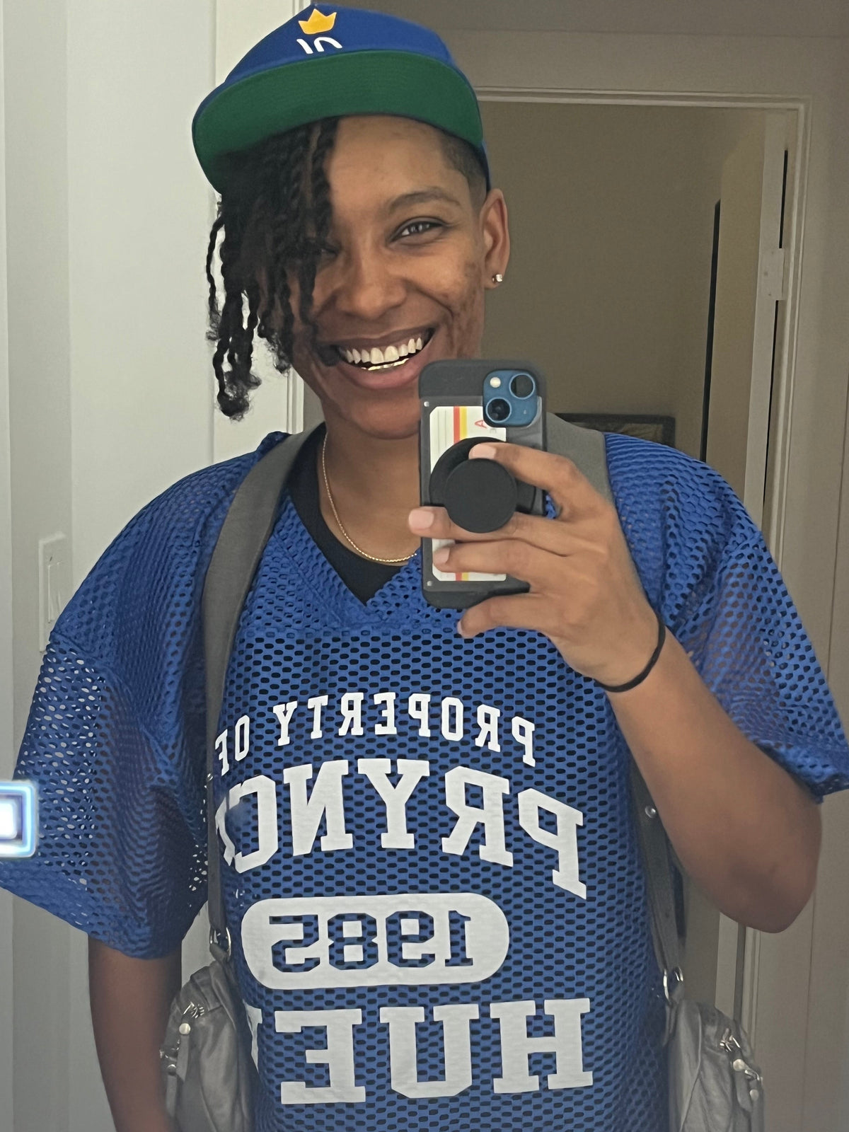 Person wearing a blue sports jersey with text, taking a mirror selfie.