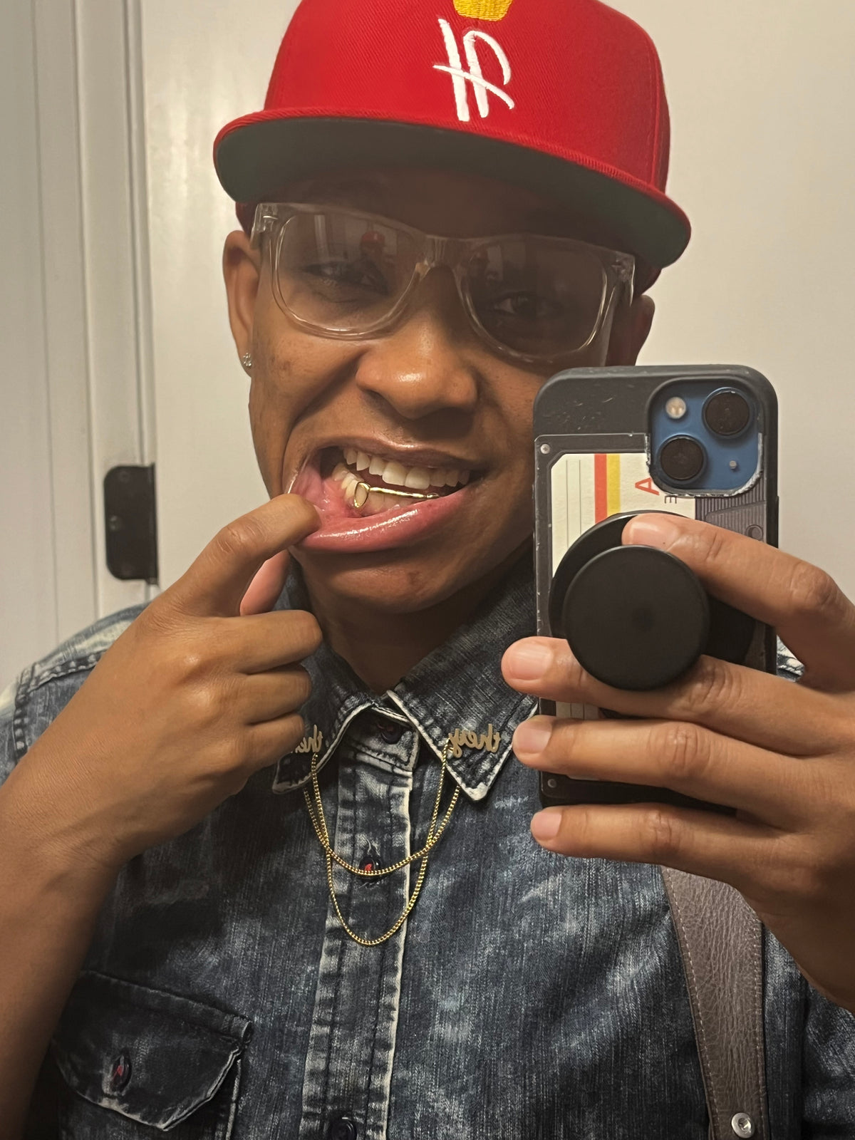 Person wearing a red cap and sunglasses, holding a phone with a visible brand logo.
